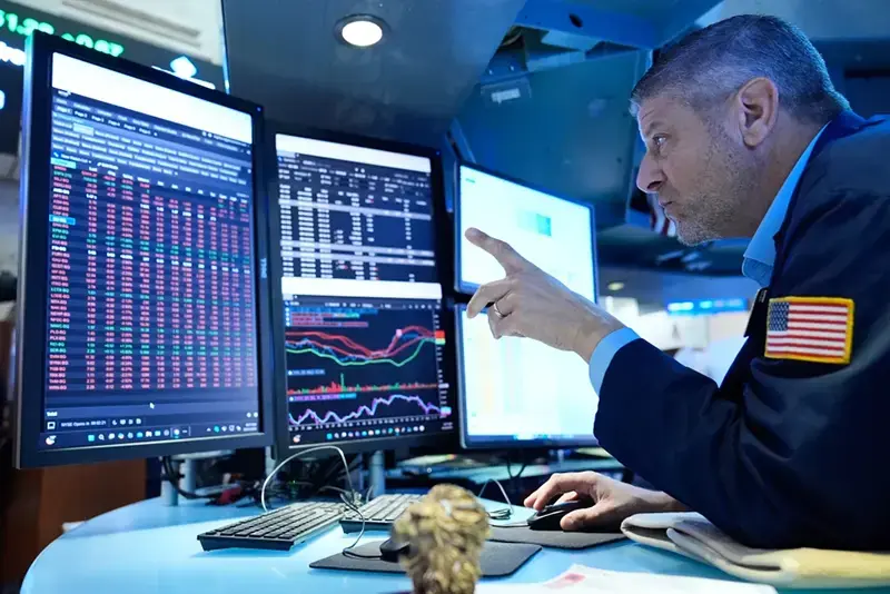 A trader is analyzing financial data on multiple computer screens in a modern trading environment.