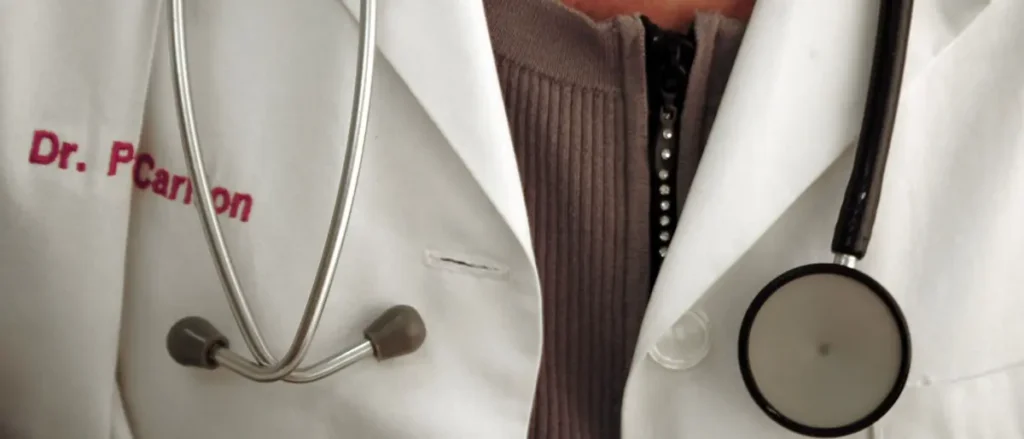 The image shows a close-up of a doctor's white coat with a stethoscope and the name "Dr. P. Carson" embroidered on it.