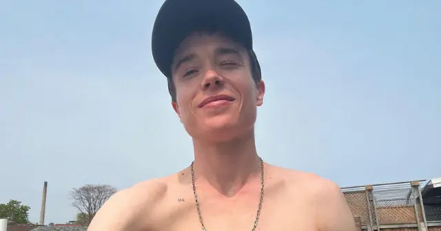 The photo shows a shirtless individual wearing a cap and a necklace, standing outdoors with a clear sky and some buildings in the background.