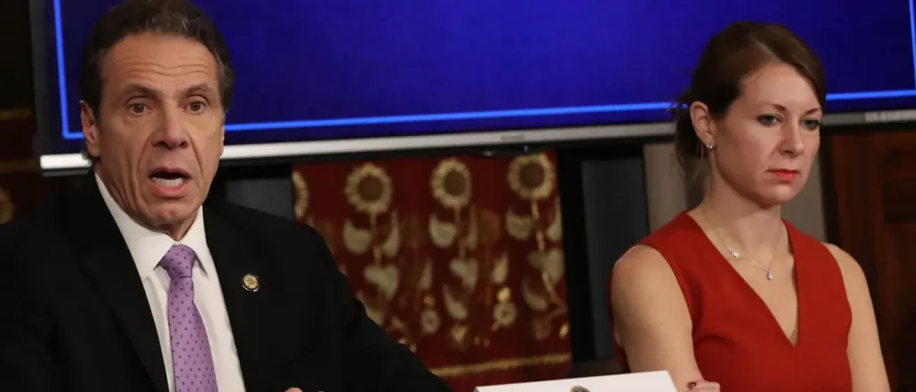 The image shows a man in a suit and a woman in a red dress, likely during a formal news or political event.