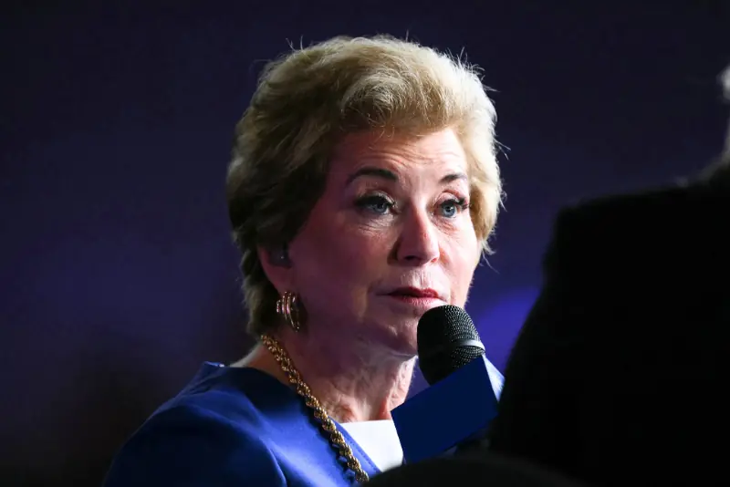 A woman in a blue suit is speaking into a microphone at a formal event.