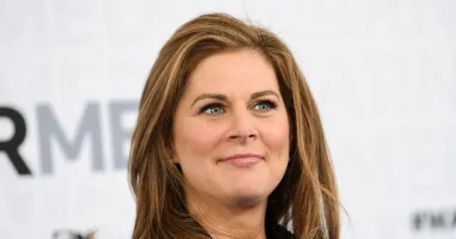 The image shows a person with long, light brown hair smiling in front of a backdrop with the letters "RMB" visible.