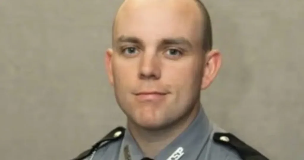 The image shows a person in a police uniform, likely a law enforcement officer, against a plain background.