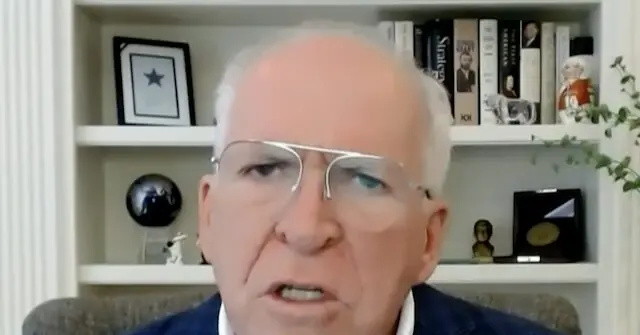 The image shows a person speaking in front of a bookshelf filled with books, framed pictures, and decorative items.