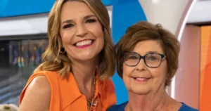 The photo features two women smiling in a studio setting, with one wearing an orange top and the other in a blue top.