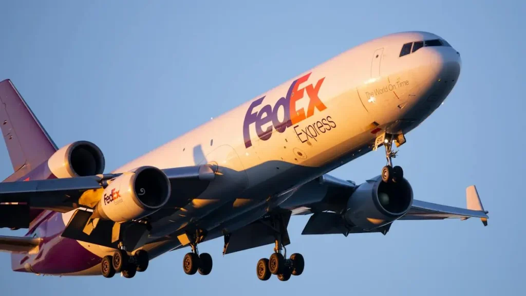 A FedEx Express cargo plane is captured in flight, with its landing gear extended, against a clear sky.