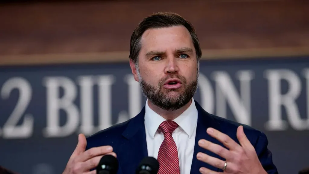 A man in a suit and tie is speaking at a press conference, with a backdrop that includes the text "2 BILLION."