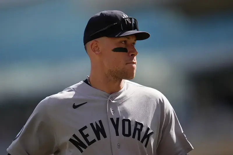 The image shows a baseball player wearing a New York Yankees uniform, standing on the field with a focused expression.