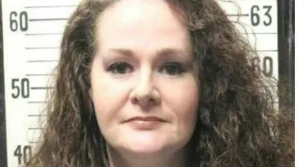 The image appears to be a mugshot of a person with curly hair, taken against a background with height measurement markings.