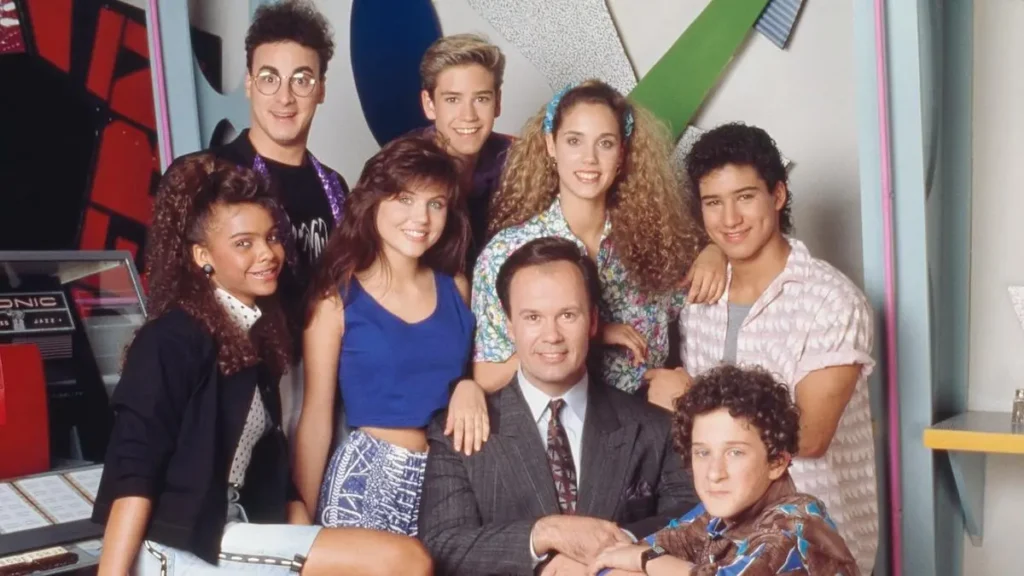 This image features a group of people posing together in a colorful, retro-styled setting, likely from a television show or promotional event.