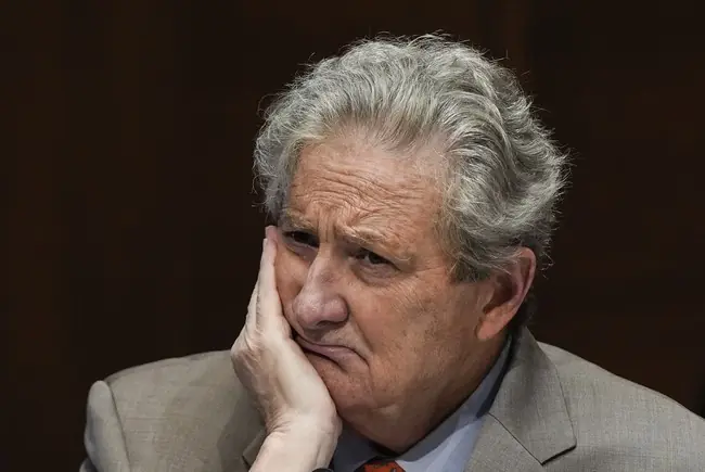 The image shows a man in a suit with his hand on his chin, appearing thoughtful or concerned.