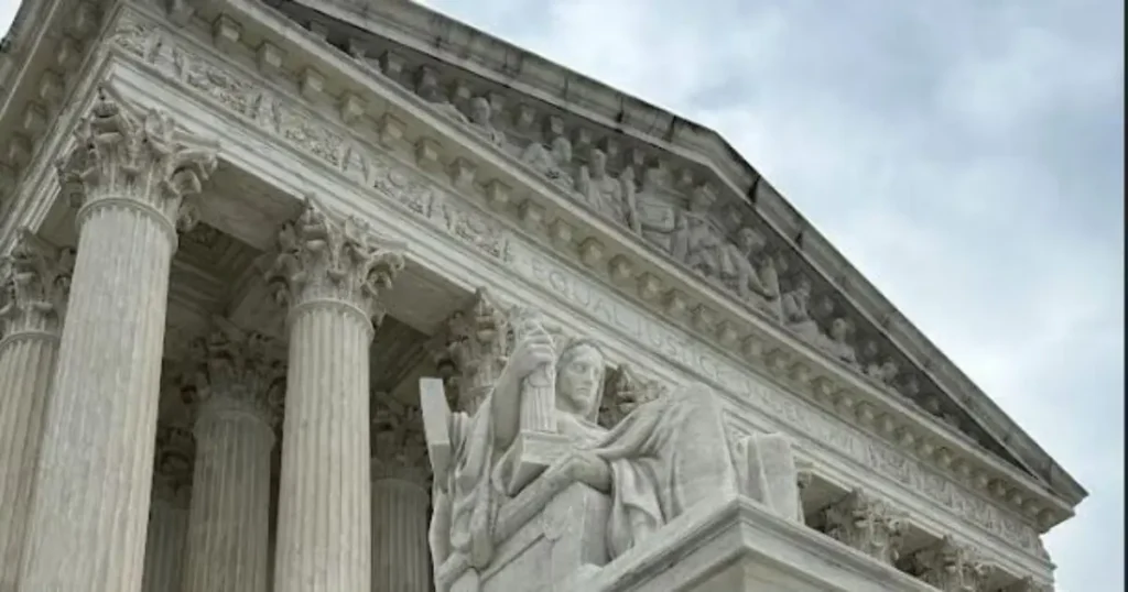 The image shows the exterior of the United States Supreme Court building, featuring intricate architectural details and a statue of a woman holding a book.