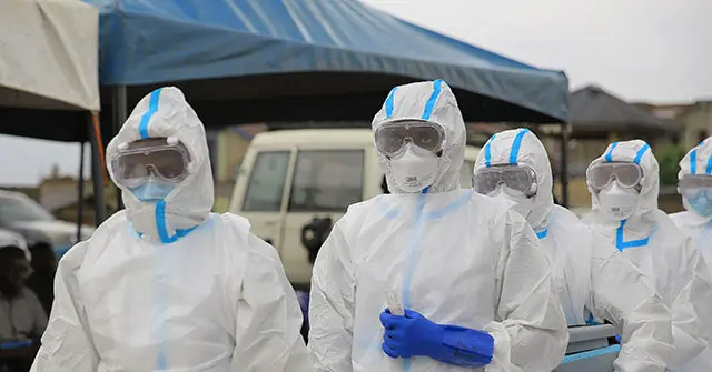 A group of healthcare workers in full protective gear stands together, ready to assist during a medical emergency.
