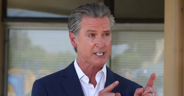 The image shows a man in a suit gesturing with his hands, likely speaking or explaining something.