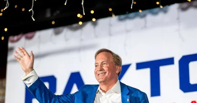A man in a blue suit waves to the crowd at a campaign event.