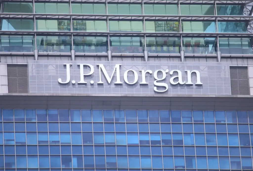 The image shows the J.P. Morgan logo prominently displayed on the facade of a modern glass building.