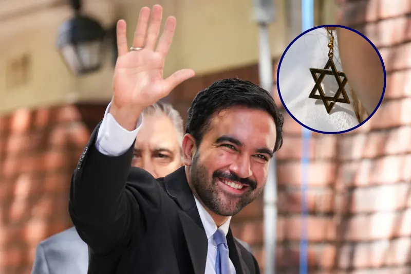 A man in a suit waves while wearing a Star of David necklace.