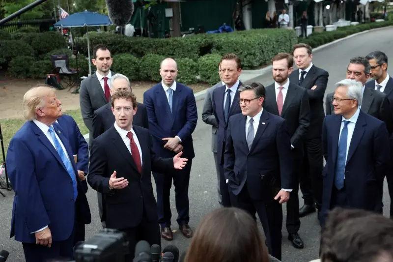 The photo shows a group of men in suits gathered outdoors, with one man speaking and others listening attentively.