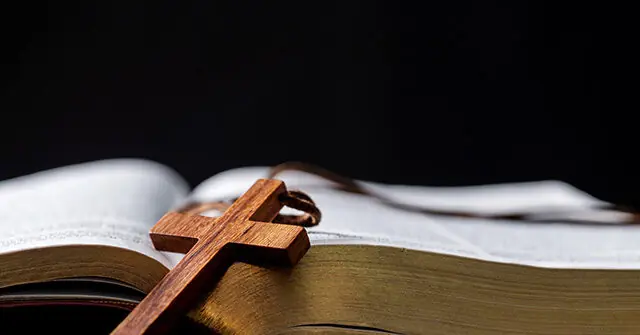 The image depicts a wooden cross resting on an open book, symbolizing faith and spirituality.