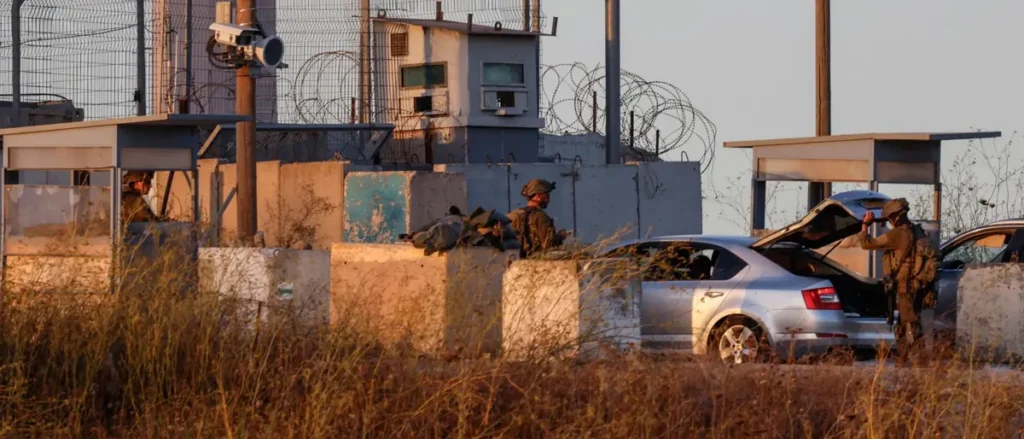 A soldier is seen interacting with a car at a checkpoint, with another soldier and a security camera visible in the background.