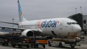 A FlyDubai aircraft is parked at an airport gate, with luggage carts and a jet bridge connected to the plane.