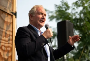 A man in a suit is speaking into a microphone at an outdoor event.