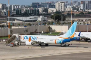 A flydubai aircraft is parked at an airport gate with a cityscape in the background.
