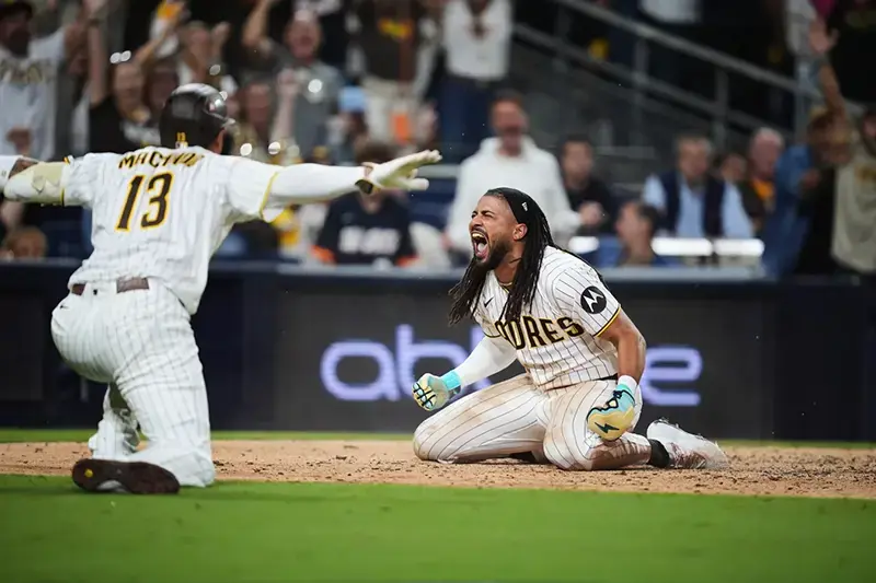 A baseball player celebrates on the ground while another player reaches out, likely in a moment of triumph or camaraderie during a game.