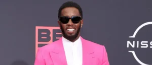 The image shows a person wearing a bright pink suit and sunglasses, standing in front of a backdrop with the BET logo.