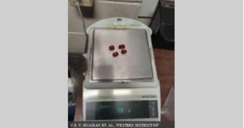 The image shows a digital scale with four red objects placed on its platform, likely in a legal or forensic context.