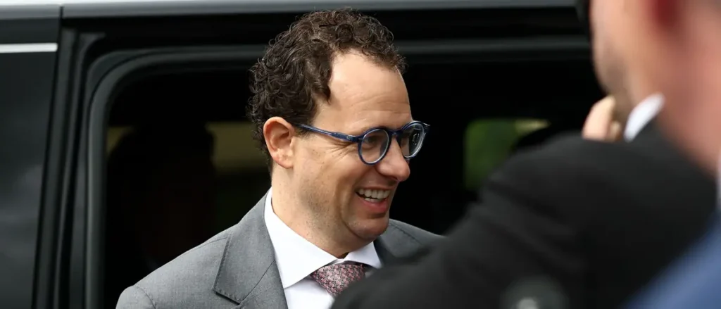 A man in a suit and glasses is smiling while standing next to a vehicle.