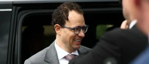 A man in a suit and glasses is smiling while standing next to a vehicle.
