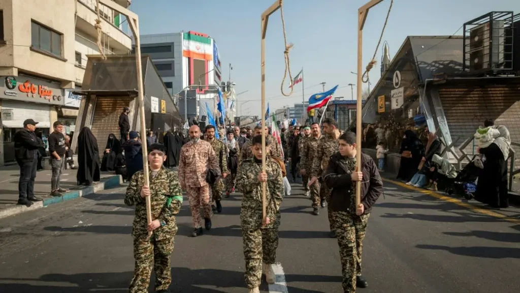 A group of individuals in military uniforms march down a street, carrying symbolic nooses, as part of a public demonstration or parade.