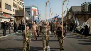 A group of individuals in military uniforms march down a street, carrying symbolic nooses, as part of a public demonstration or parade.