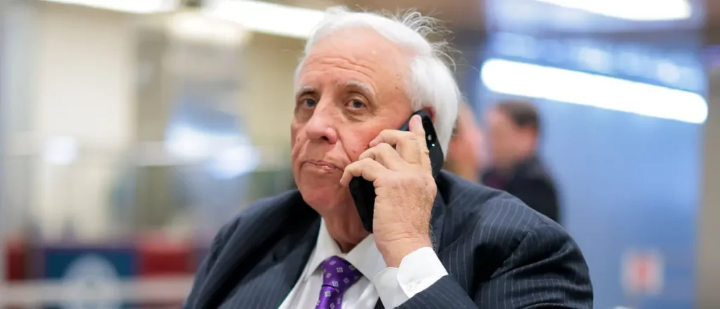 An older man in a suit and tie is engaged in a phone conversation in a professional setting.
