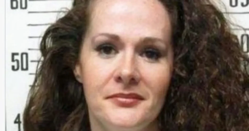 The image appears to be a mugshot of a woman with curly hair, taken in a police station setting.