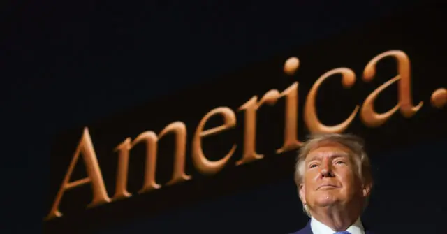 The image shows a person standing in front of a large, illuminated sign that reads "America."