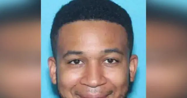 The image is a news photo of a man with short hair, smiling, set against a blue background.