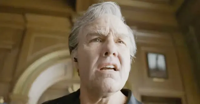 The image shows a person with white hair looking upwards in a grand, possibly historical, setting with arched architecture and a window in the background.