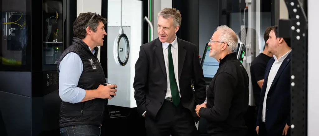A group of men in professional attire are engaged in conversation in a modern industrial setting.