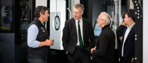 A group of men in professional attire are engaged in conversation in a modern industrial setting.