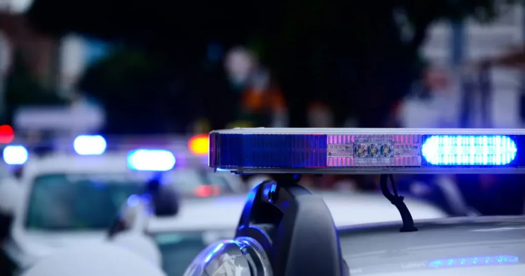 The image shows a police car with flashing blue lights, indicating an emergency or active scene.