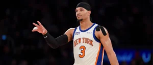The image shows a basketball player wearing a New York Knicks jersey, number 3, with a black headband and a black arm sleeve, gesturing with his hand.