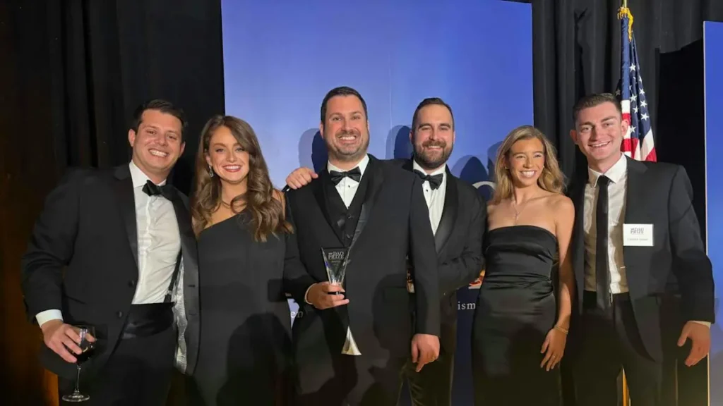 A group of six people, dressed in formal attire, pose for a photo holding an award at what appears to be a formal event.
