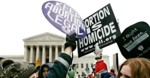 The photo depicts a protest in front of a government building, with signs advocating for and against abortion rights.