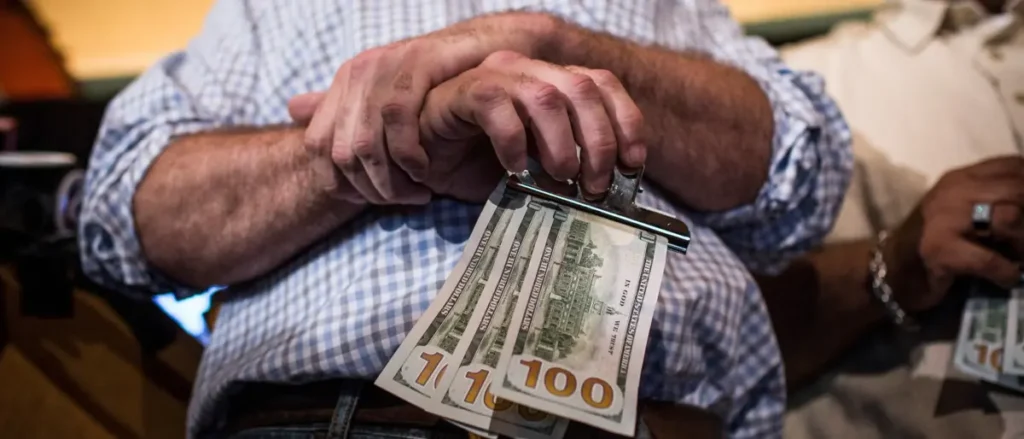 An elderly man holds a stack of $100 bills, symbolizing financial security or a significant financial transaction.