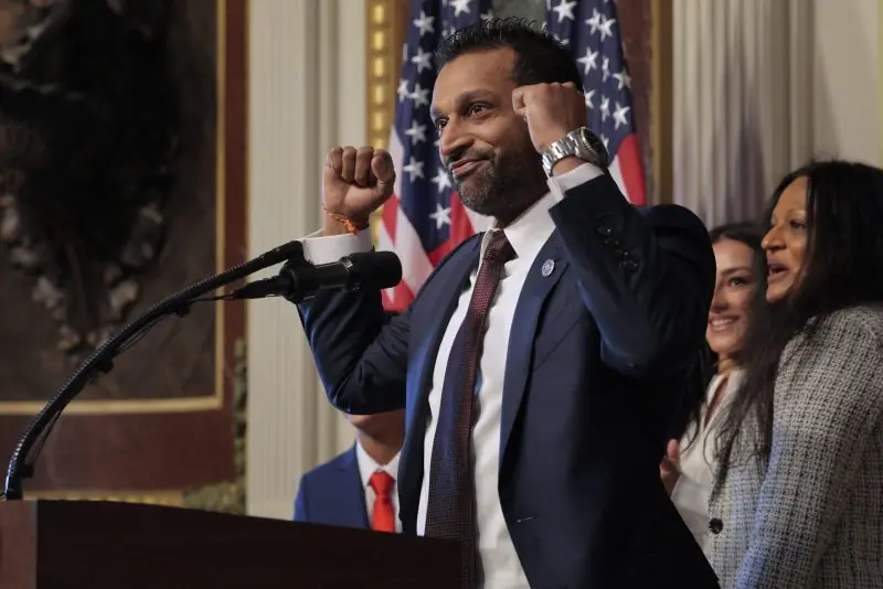 A man in a suit raises his fist in a gesture of solidarity or triumph at a podium with an American flag in the background.