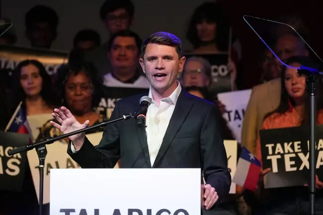 A man stands at a podium with a sign that reads "TALARICO," addressing a crowd holding signs that say "TAKE BACK TEXAS."