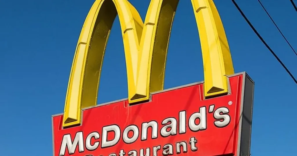 The image shows a McDonald's restaurant sign with the iconic golden arches and red background against a clear blue sky.