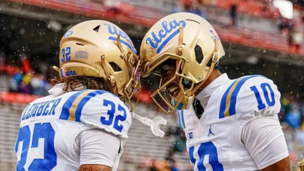 Two UCLA football players celebrate on the field during a rainy game.